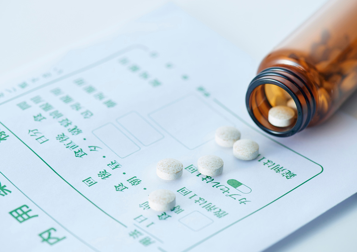 処方箋の上に白い錠剤が散らばり、茶色の薬瓶が横に倒れている
